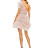 A woman in a light pink Tulle Ruffle One Shoulder Mini Dress with floral detail stands in heels on a white background, facing away.